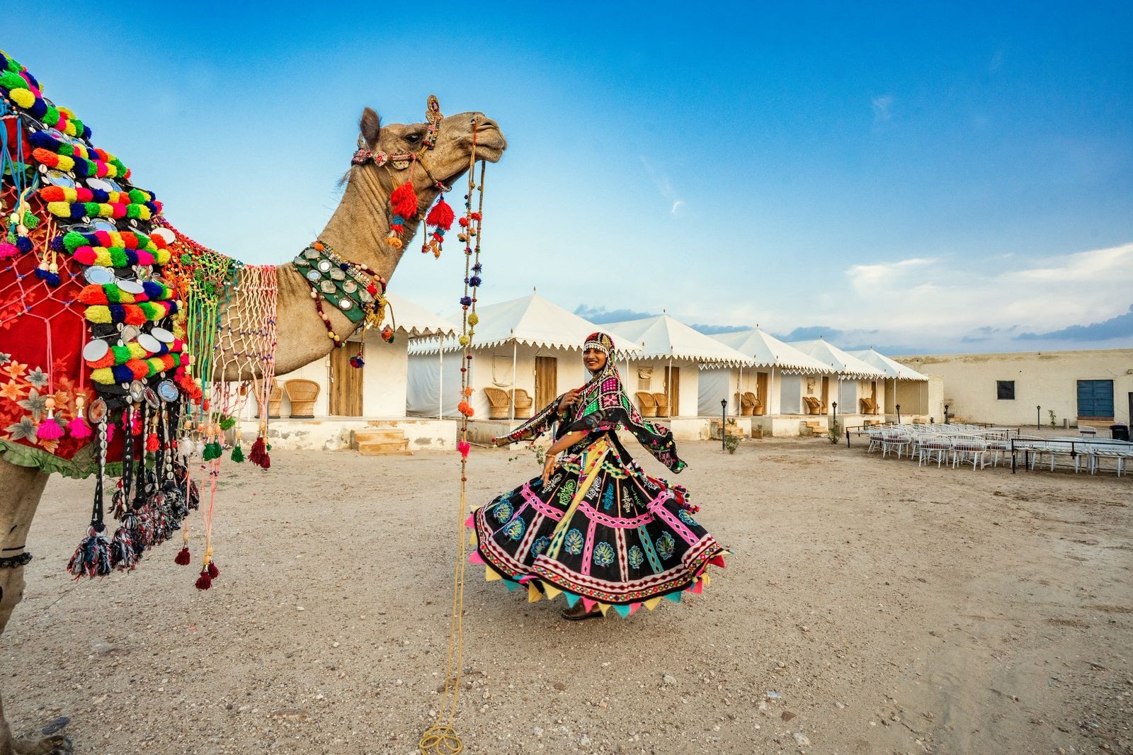 Authentic Kalbelia folk dancer in traditional mirror-work dress with decorated camel at desert camp